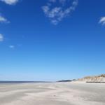 Weiterer Strandabschnitt mit Dünen und blauem Himmel.
