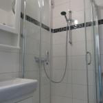 Duschkabine mit Glaswand, weißer Fliesenwand und Handdusche.
