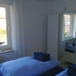Zimmer mit Bett, Spiegel und Fenster. Auf dem Fensterbrett stehen dekorative Gegenstände.