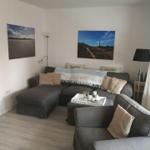 Wohnzimmer mit grauem Sofa, Wandbildern und Holzboden.