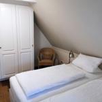 Schlafzimmer mit Doppelbett, weißen Bettwäsche, Schrank und Stuhl unter Dachschräge.
