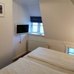 Schlafzimmer mit Dachschrägen, Bett, Fernseher und Fenster.