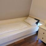 Ein Schlafzimmer mit einem weißen Bett, einem Nachttisch und einer Lampe.