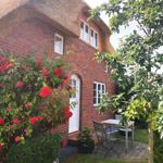 Rotes Backsteingebäude mit Strohdach, Rosen an der Wand und Gartenmöbel auf Steinplatten.