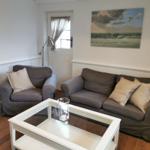 Wohnzimmer mit grauem Sofa, Sessel und Glas-Tisch. Wandbild zeigt Meereslandschaft.