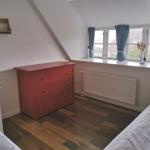 Schlafzimmer mit rotem Schrank, Holzboden und Fenster mit blauen Vorhängen.