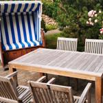 Terrasse mit Holztisch, Stühlen und Strandkorb mit blau-weißem Streifenmuster.