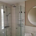 Dusche mit Glaswand, runder Spiegel und Handtuch auf Waschtisch.