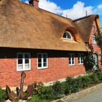 Rotes Backsteinhaus mit Strohdach und Fenstern. Vorgarten mit Blumen und Anker.