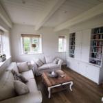Wohnzimmer mit weißen Sofas, Holztisch und Bücherregal an der Wand.