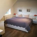 Schlafzimmer mit Dachschräge, Bett, zwei Nachttischen und Fenster.