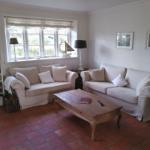 Wohnzimmer mit zwei Sofas, Holztisch und Fenster. Terrakottaboden und weiße Wände.