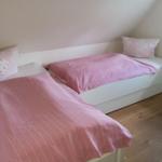 Zwei Betten mit rosa Bettwäsche und Kissen in einem Zimmer mit Holzboden und Fenster.