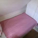 Schlafzimmer mit Bett, rosa Bettwäsche und weißem Schrank.