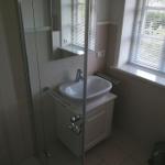 Badezimmer mit Dusche, Waschbecken und Fenster mit Jalousie.