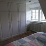 Schlafzimmer mit Kleiderschrank, Fenster und Bett mit buntem Decken.