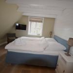 Schlafzimmer mit Doppelbett, Fenster und Fernseher an der Wand.