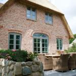 Haus mit Strohdach, Steinmauer, Sitzgruppe und Gartentisch.