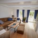 Wohnzimmer mit braunem Sofa, Holztisch und blauen Vorhängen vor Fenstern.
