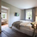 Schlafzimmer mit Bett, TV und Fenster. Holzfußboden und Nachttisch mit Lampe.