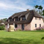 Ein Haus mit strohgedecktem Dach und Backsteinfassade steht auf einer grünen Wiese.