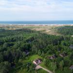 Haus mit Garten, umgeben von Wald und Strand im Hintergrund.