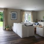 Wohnzimmer mit weißem Sofa, Holzboden und Blick auf Garten.