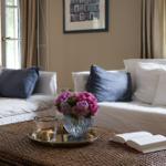 Wohnzimmer mit weißen Sofas, blauen Kissen und einem Korbtablett mit Blumen und Buch.