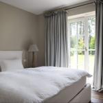 Schlafzimmer mit weißem Bett und Fenster zur grünen Außenseite.
