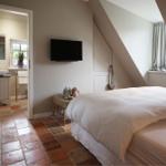 Schlafzimmer mit Dachschrägen, Bett, Fernseher und Tür zum Badezimmer.