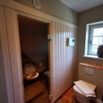 Sauna mit Holzwand, Toilette und Fenster mit Blumenkorb.
