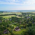 Luftbild einer ländlichen Gegend mit Häusern, Wiesen und Meer im Hintergrund.
