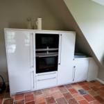 Küche mit weißer Einbauküche und integriertem Backofen unter schrägem Dach.