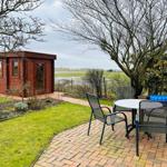 Holzhaus mit Garten, Tisch und Stühlen. Blick auf Felder und Bäume.