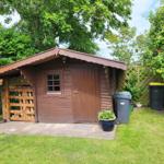 Holzgarage mit Dachüberstand und Mülltonnen im Garten.