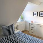 Schlafzimmer mit Dachschräge, Bett mit Streifen, Schrank und Bilder an der Wand.