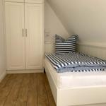 Schlafzimmer mit weißem Bett und Streifenbezug, Holzboden und weißen Schränken unter schräger Decke.