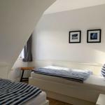 Zimmer mit zwei Betten, schräger Decke und Fenster mit Vorhang.