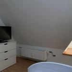 Zimmer mit schrägen Wänden, Fernseher, Heizkörper und Fenster