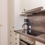 Küche mit Kochfeld, Kaffeemaschine und Holzrückwand.