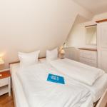 Schlafzimmer mit Doppelbett, Nachttisch, Kleiderschrank und Schreibtisch.