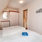 Schlafzimmer mit Doppelbett, Kleiderschrank und Bücherregal. Tür führt zur Treppe.