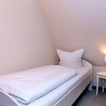 Ein Schlafzimmer mit Einzelbett, Nachttisch und Lampe. Die Wände sind hell gestrichen.