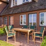 Terrasse mit Holztisch und grünen Stühlen vor einem Backsteinhaus mit Strohdach.