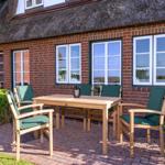 Terrasse mit Holztisch und Stühlen vor einem roten Backsteinhaus mit Strohdach.