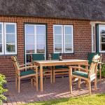 Terrasse mit Holztisch und Stühlen vor einem Backsteinhaus mit Strohdach.