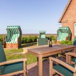 Terrasse mit Holztisch, Stühlen und Strandkörben. Blick auf Grünfläche und Haus.