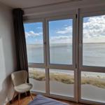 Zimmer mit Blick auf Strand und Meer durch große Fenster.
