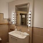 Bad mit Waschbecken, Spiegel mit Licht und Dusche im Hintergrund.