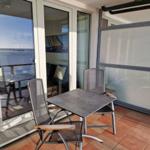 Terrasse mit Tisch und zwei Stühlen, Glaswand und Blick auf das Meer.